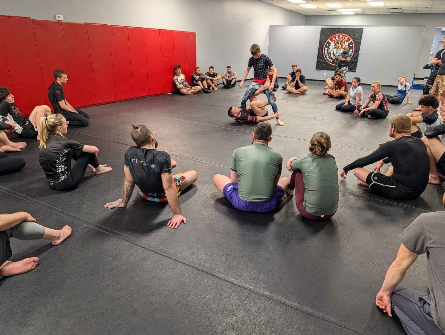 Instructor demonstrating a technique to students seated on the mats
